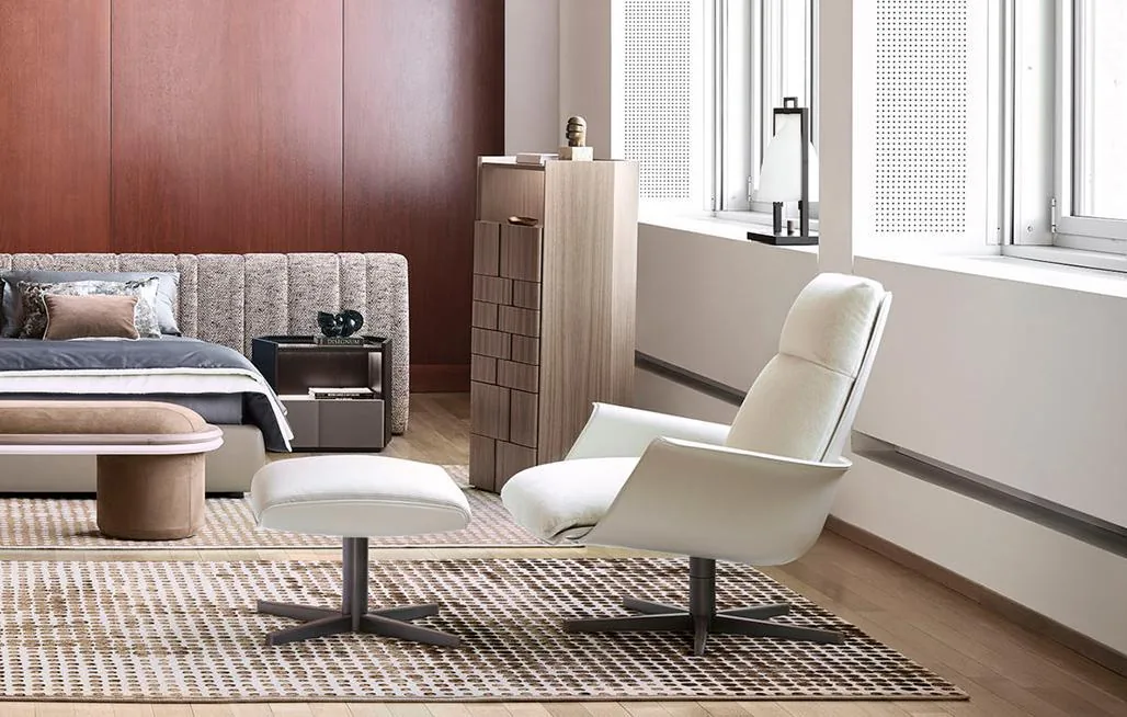 A pale high-back lounge chair on a dark four-point base beside a window.