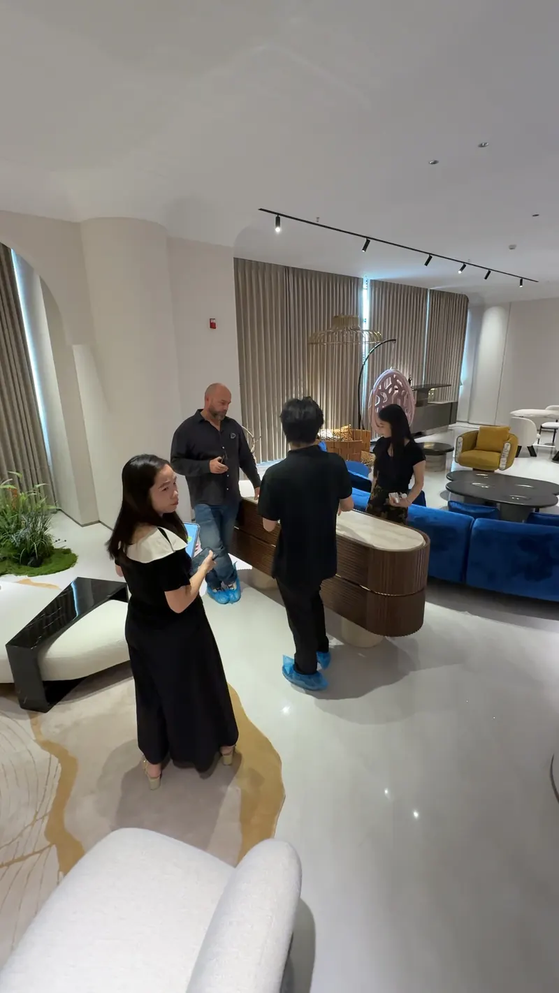 Four adults stand around a low cabinet near a blue sofa in a furniture showroom.