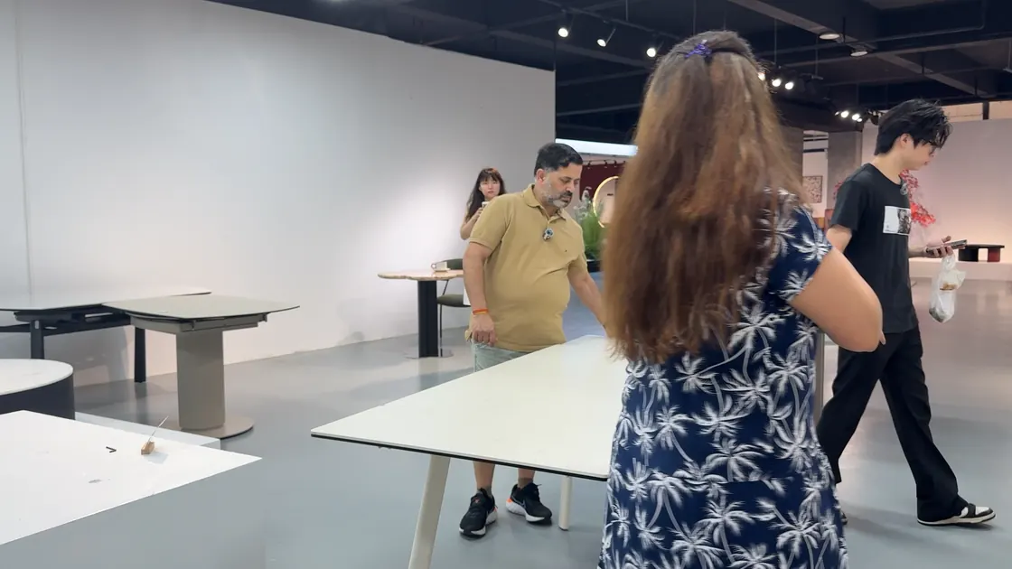 People walk among pale table displays in an open showroom.